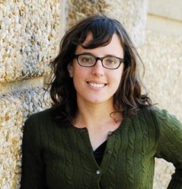 Bio photo of Arin Greenwood, smiling in a green shirt standing in front of rough stone wall